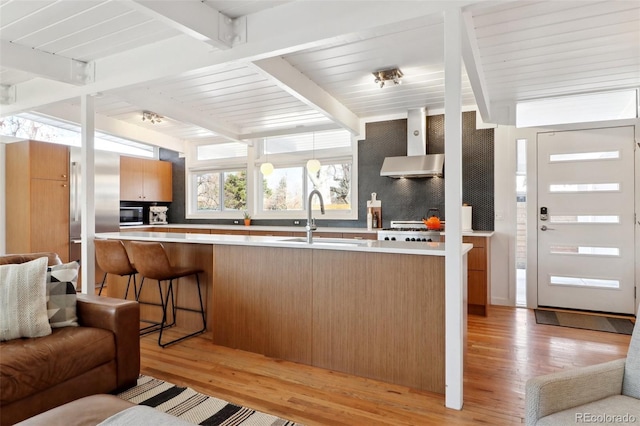 kitchen featuring beamed ceiling, wall chimney exhaust hood, light wood-type flooring, and a sink