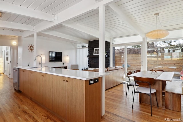 kitchen with light wood finished floors, an island with sink, a sink, open floor plan, and light countertops