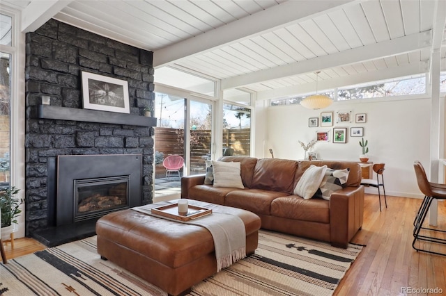 living area featuring light wood-type flooring, beamed ceiling, baseboards, and a stone fireplace