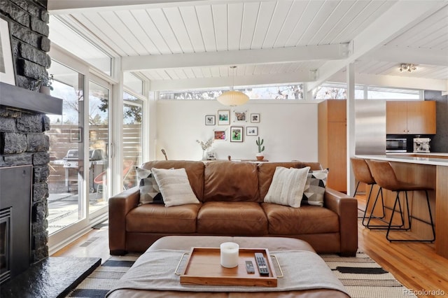 living room with plenty of natural light, a fireplace, lofted ceiling with beams, and light wood-style floors