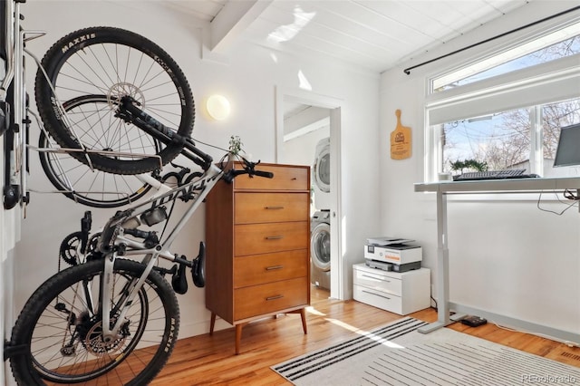 misc room featuring beamed ceiling, stacked washer and clothes dryer, and light wood-style floors