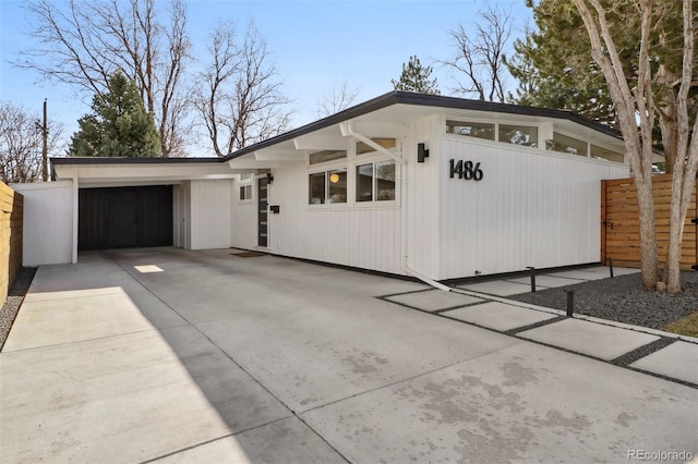 mid-century inspired home featuring concrete driveway and fence