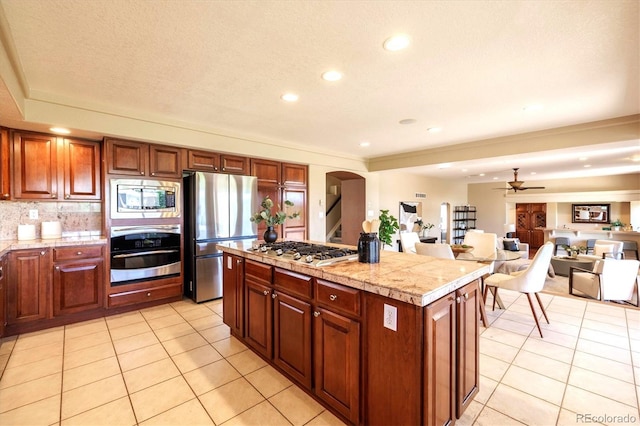 10085 Charissglen Ct, Highlands Ranch, CO 80126 - kitchen with appliances with stainless steel finishes, ceiling fan, light tile patterned floors, arched walkways, and a kitchen island