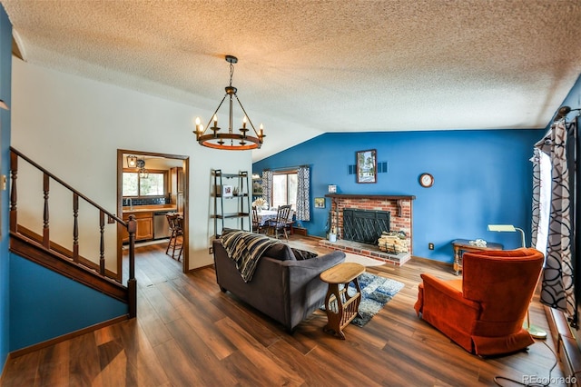 living room with a brick fireplace, a textured ceiling, vaulted ceiling, hardwood / wood-style flooring, and a chandelier