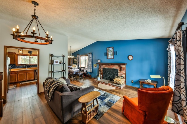 living room featuring lofted ceiling, dark wood-type flooring, sink, a brick fireplace, and a chandelier