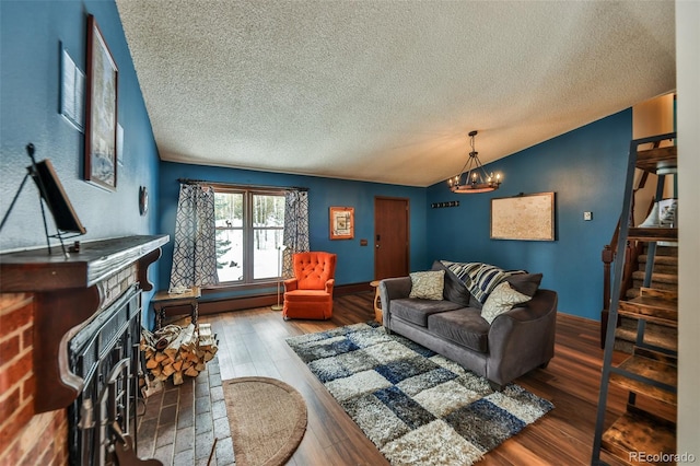 living room featuring a brick fireplace, a textured ceiling, a notable chandelier, hardwood / wood-style floors, and lofted ceiling