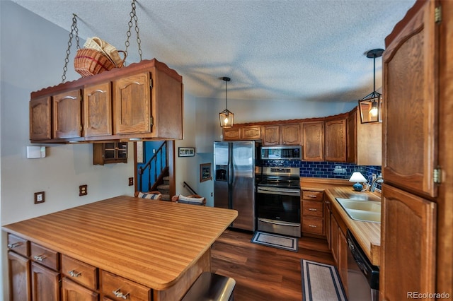 kitchen with lofted ceiling, hanging light fixtures, decorative backsplash, a textured ceiling, and appliances with stainless steel finishes