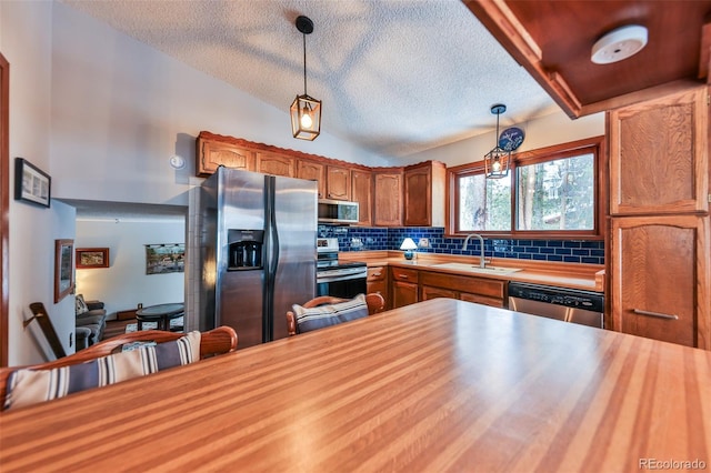 kitchen with lofted ceiling, sink, hanging light fixtures, decorative backsplash, and stainless steel appliances