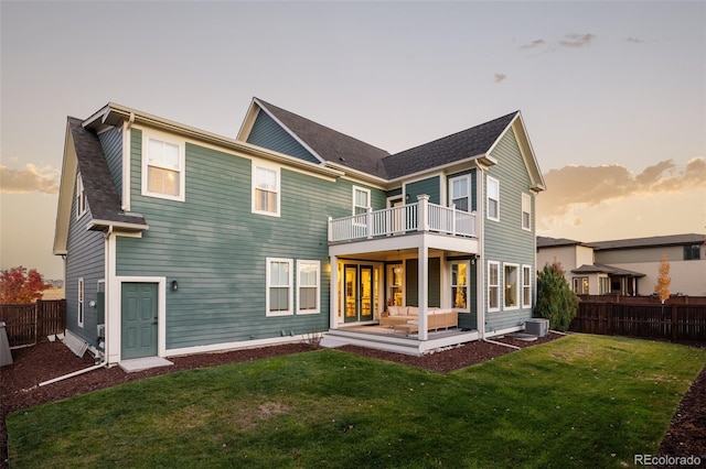 back house at dusk with an outdoor hangout area, cooling unit, a balcony, and a yard