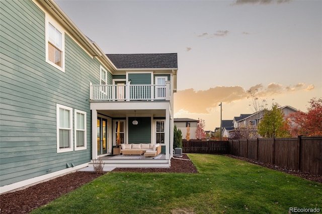 back house at dusk featuring a yard, outdoor lounge area, a patio area, and a balcony