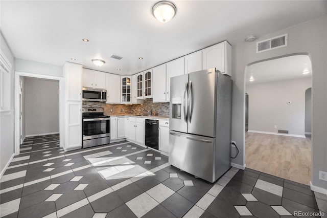 1560 Pueblo Ct, Thornton, CO 80229 - kitchen featuring appliances with stainless steel finishes, arched walkways, dark tile patterned flooring, tasteful backsplash, and glass insert cabinets