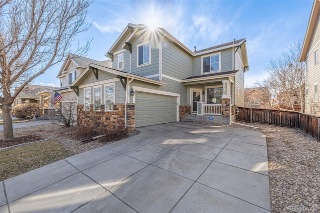 traditional home featuring a garage, covered porch, fence, concrete driveway, and stone siding