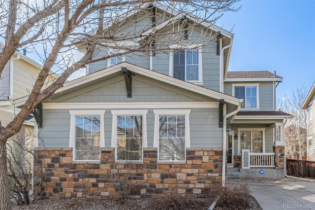 view of front of house with stone siding, a shingled roof, and fence