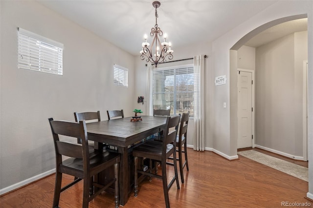 dining space featuring light wood-type flooring, baseboards, arched walkways, and a notable chandelier