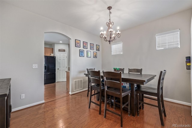 dining space with arched walkways, visible vents, an inviting chandelier, wood finished floors, and baseboards