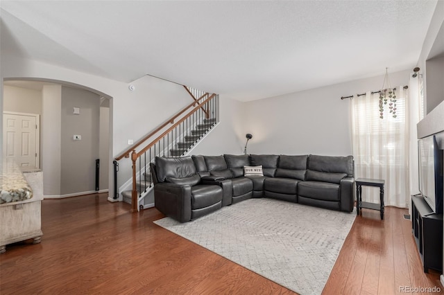 living area with stairs, arched walkways, wood finished floors, and baseboards