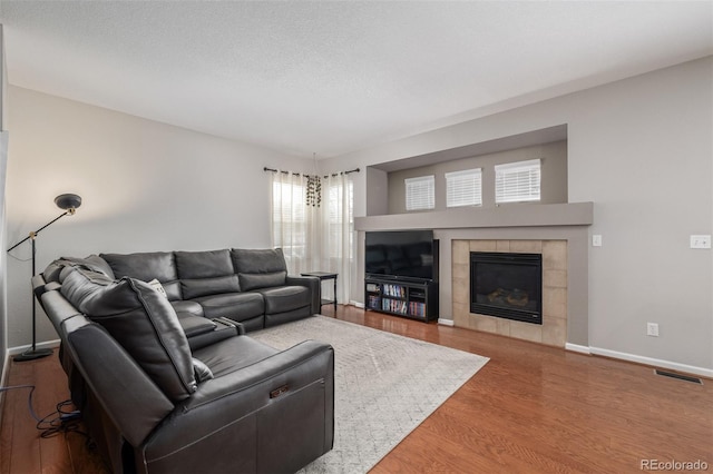 living area with a textured ceiling, wood finished floors, visible vents, baseboards, and a tiled fireplace