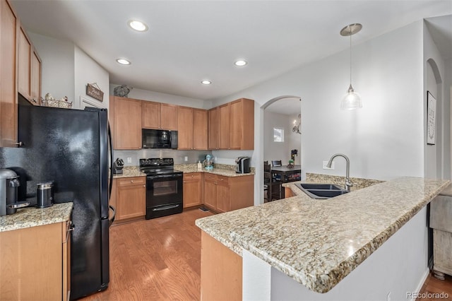 kitchen featuring a peninsula, black appliances, arched walkways, and a sink