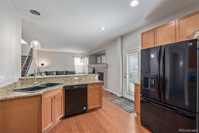 kitchen featuring light wood-style flooring, open floor plan, a peninsula, black appliances, and a sink