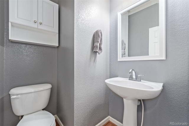 half bath featuring baseboards, a textured wall, a sink, and toilet