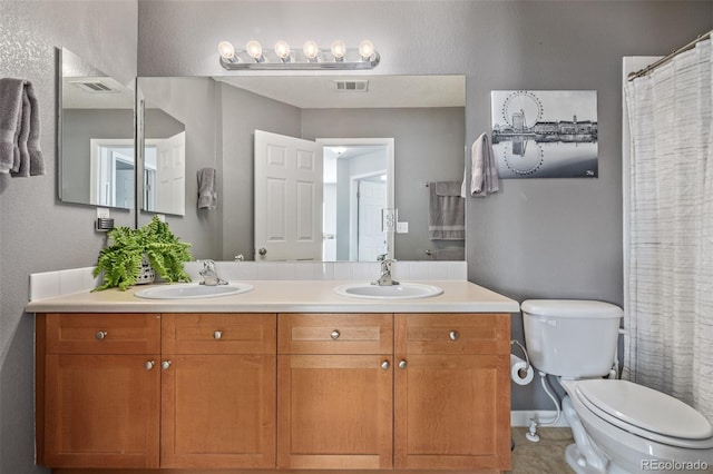 bathroom featuring toilet, double vanity, visible vents, and a sink