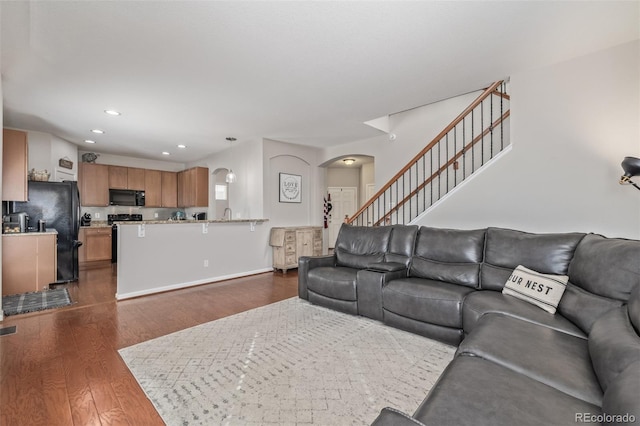 living room featuring arched walkways, recessed lighting, dark wood-type flooring, baseboards, and stairs