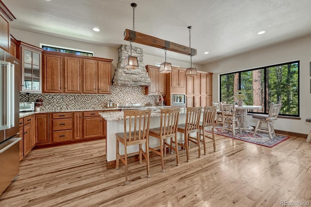 1250 Cottontail Trl, Woodland Park, CO 80863 - kitchen featuring premium range hood, light wood-type flooring, brown cabinets, decorative backsplash, and a breakfast bar