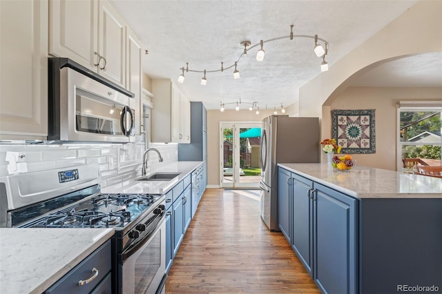 kitchen with white cabinets, blue cabinets, appliances with stainless steel finishes, and sink