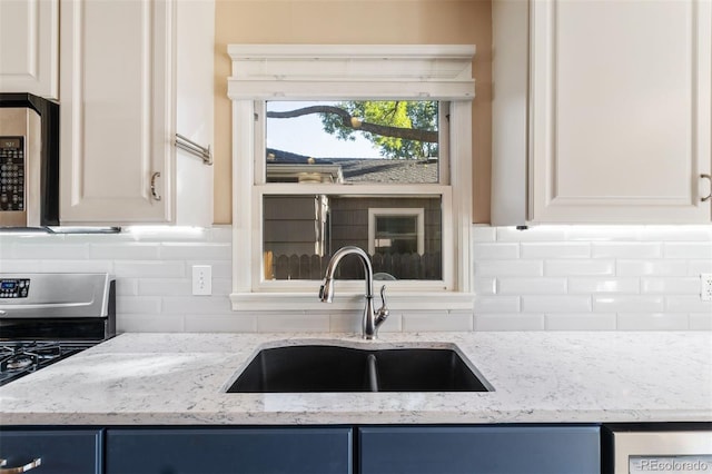 kitchen with light stone countertops, appliances with stainless steel finishes, decorative backsplash, blue cabinetry, and sink