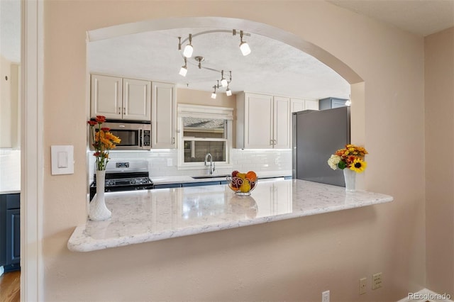 kitchen featuring sink, tasteful backsplash, white cabinetry, light stone countertops, and stainless steel appliances