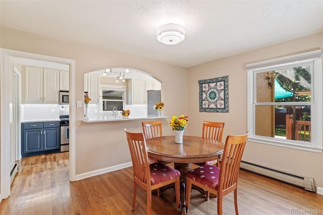 dining area with sink, light wood-type flooring, and a baseboard heating unit