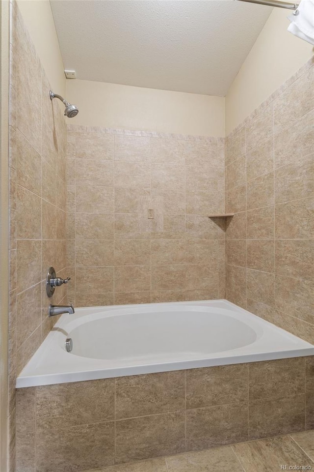 bathroom with a textured ceiling and tiled shower / bath combo