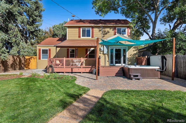 back of house featuring a wooden deck, a hot tub, a lawn, and a patio