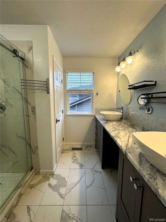 bathroom with a marble finish shower, marble look tiles, a textured ceiling, double vanity, and baseboards