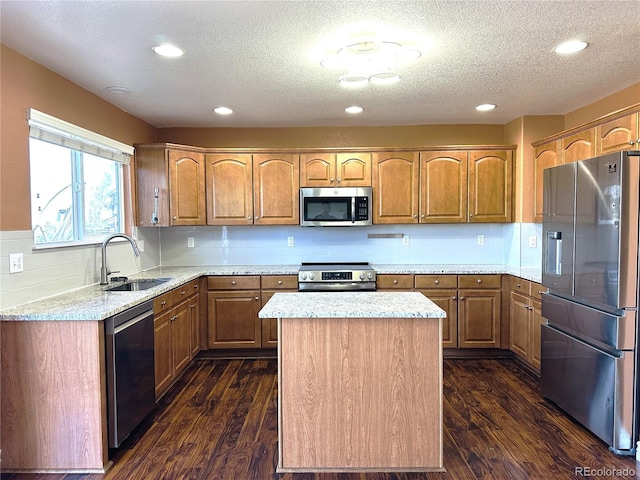 kitchen featuring appliances with stainless steel finishes, a sink, a textured ceiling, dark wood-style floors, and a kitchen island