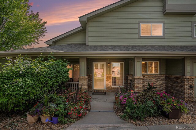 2900 Purcell St Unit 6, Brighton, CO 80601 - exterior entry at dusk with a porch, brick siding, and roof with shingles