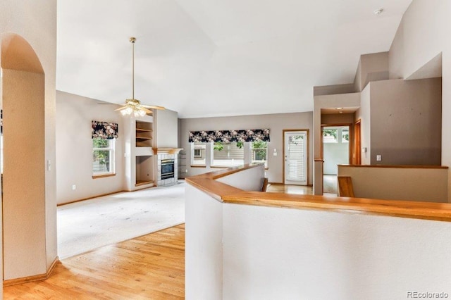 kitchen featuring baseboards, lofted ceiling, light wood-style flooring, a fireplace, and ceiling fan