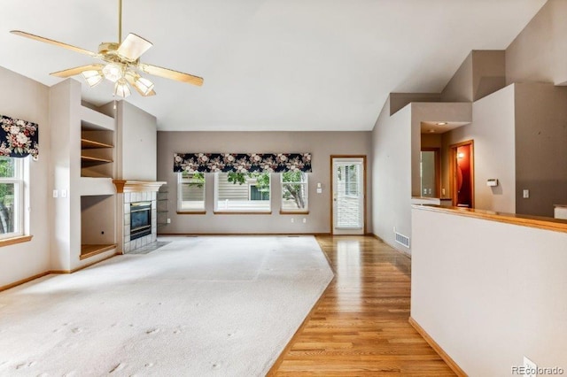 unfurnished living room with light wood-type flooring, a healthy amount of sunlight, a tile fireplace, and vaulted ceiling