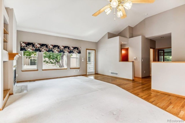 unfurnished living room featuring a ceiling fan, carpet, wood finished floors, visible vents, and a fireplace with flush hearth