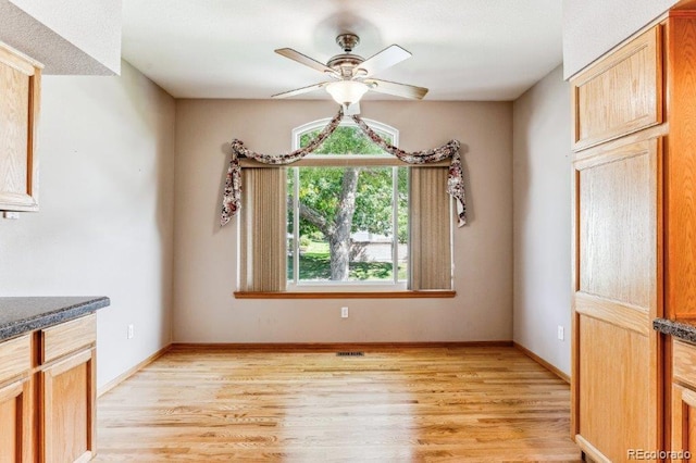 unfurnished dining area with light wood finished floors, ceiling fan, and baseboards