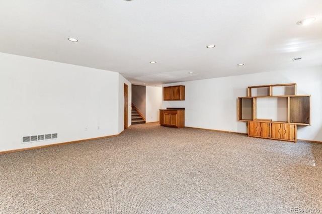 unfurnished living room featuring stairway, baseboards, light colored carpet, and visible vents