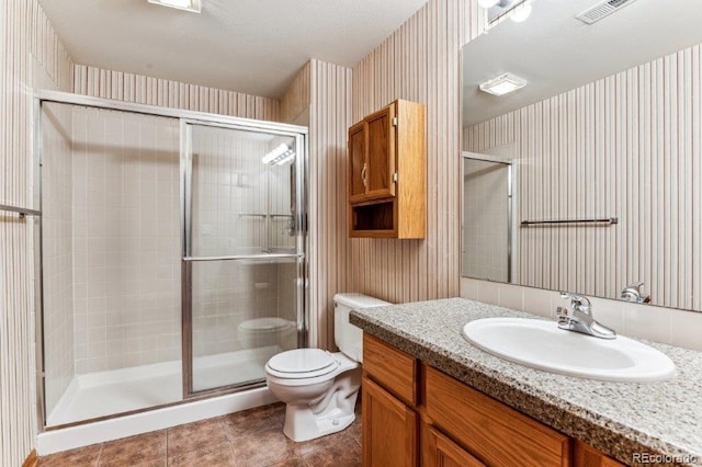 bathroom featuring vanity, visible vents, wallpapered walls, a stall shower, and toilet