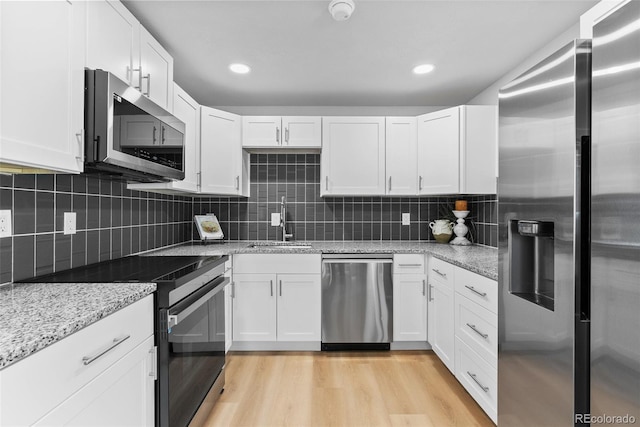 8333 Depew Way, Arvada, CO 80003 - kitchen with stainless steel appliances, a sink, white cabinetry, light stone countertops, and light wood finished floors