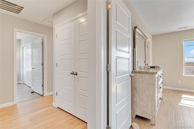 corridor featuring visible vents, baseboards, and light wood finished floors