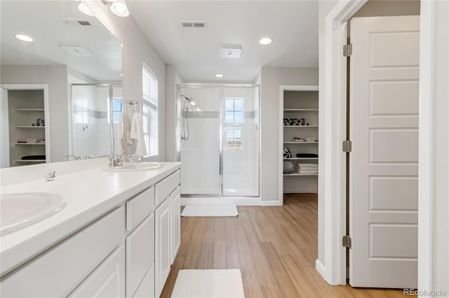 full bath featuring wood finished floors, visible vents, a sink, a shower stall, and a walk in closet