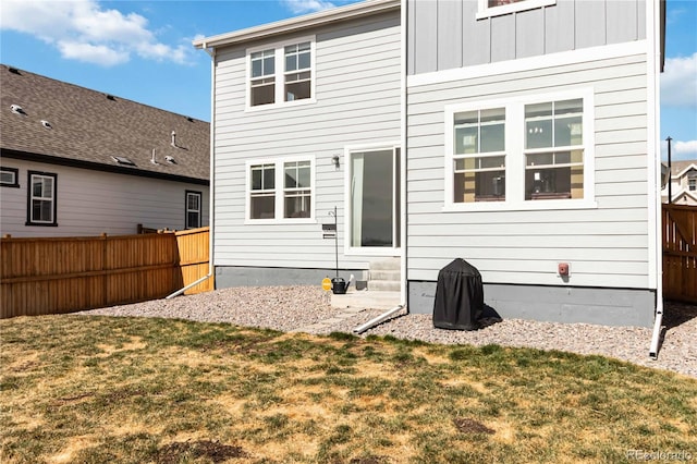 rear view of property featuring a lawn, board and batten siding, entry steps, and fence