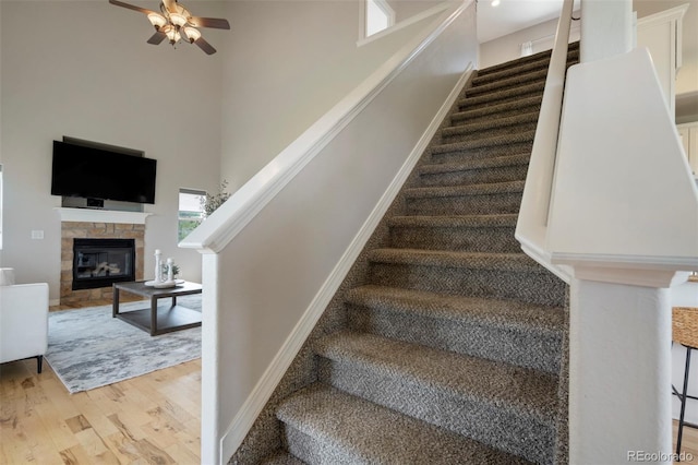 15580 Rigge Ct, Elbert, CO 80106 - stairway with wood finished floors, ceiling fan, a glass covered fireplace, a high ceiling, and baseboards