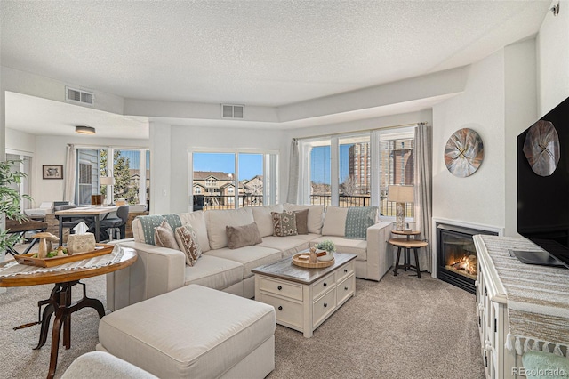 living area featuring light carpet, visible vents, a textured ceiling, and a glass covered fireplace