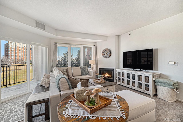 living area featuring carpet, visible vents, a glass covered fireplace, and a textured ceiling