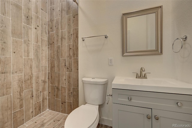 full bathroom with a tile shower, toilet, and vanity